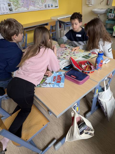 Vier Kinder sitzen an einem Tisch und betrachten gemeinsam eine große Landkarte in einem Klassenzimmer.